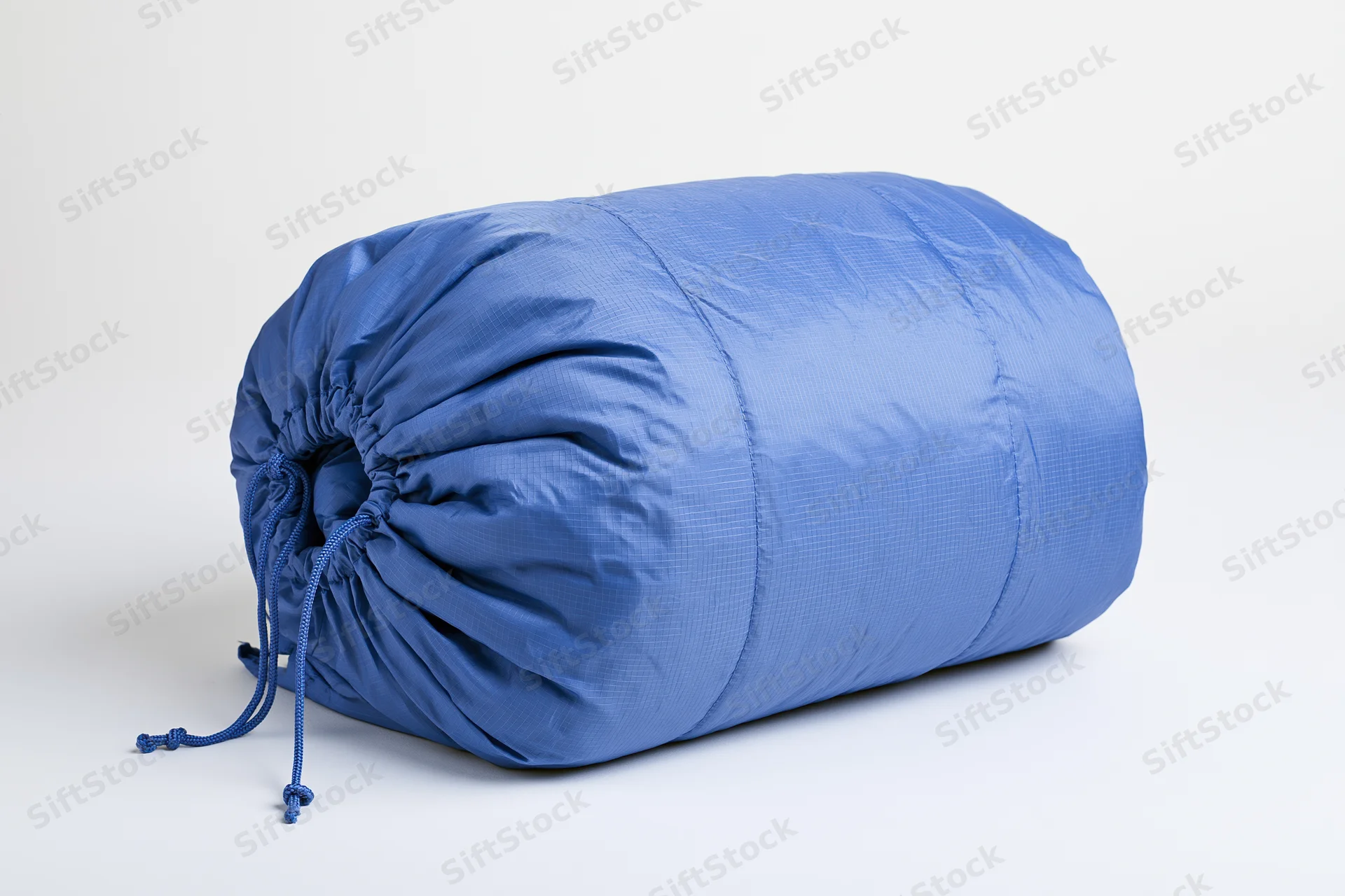 Blue nylon sleeping bag rolled and packed tightly with drawstring on white background