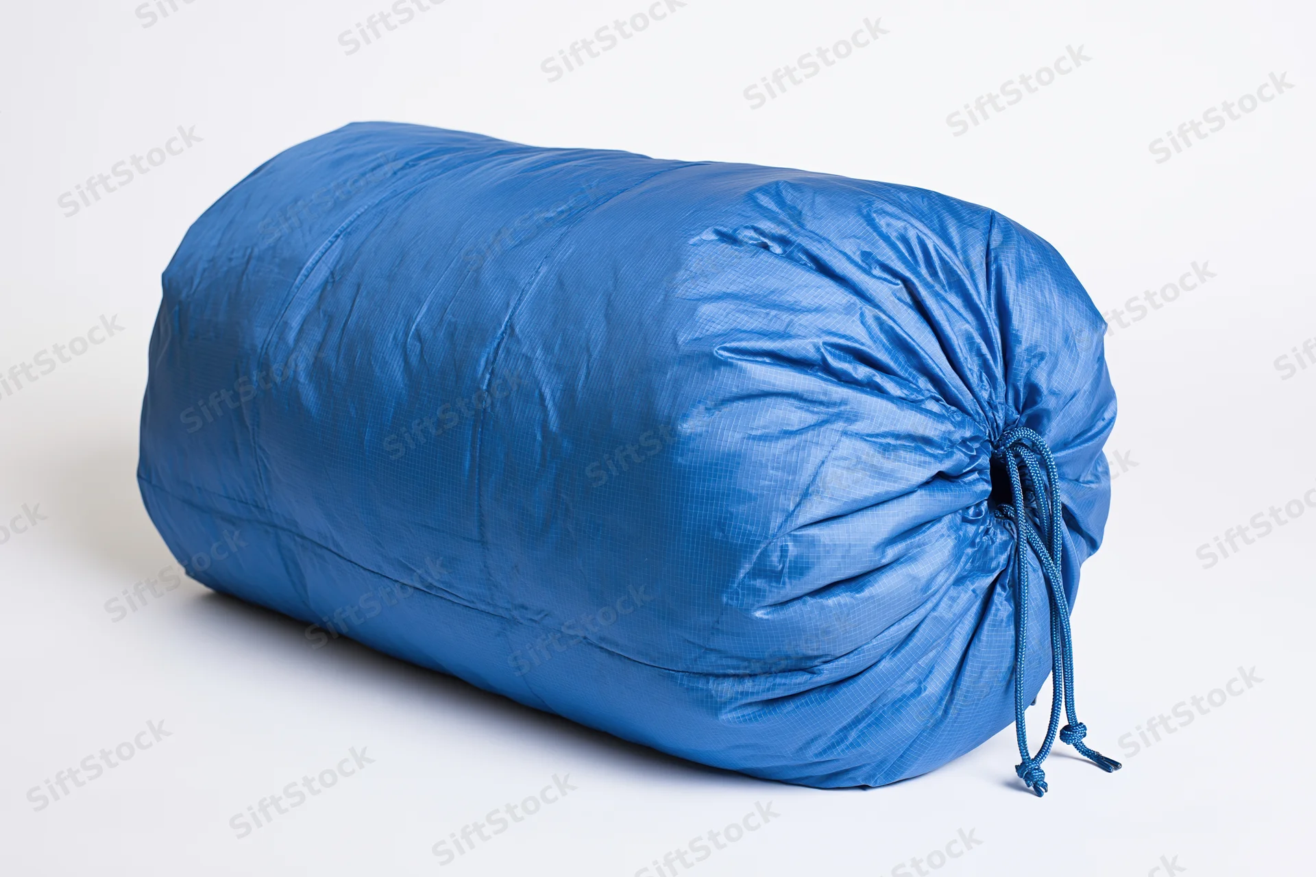 Blue nylon sleeping bag rolled and packed tightly with drawstring closure on white background