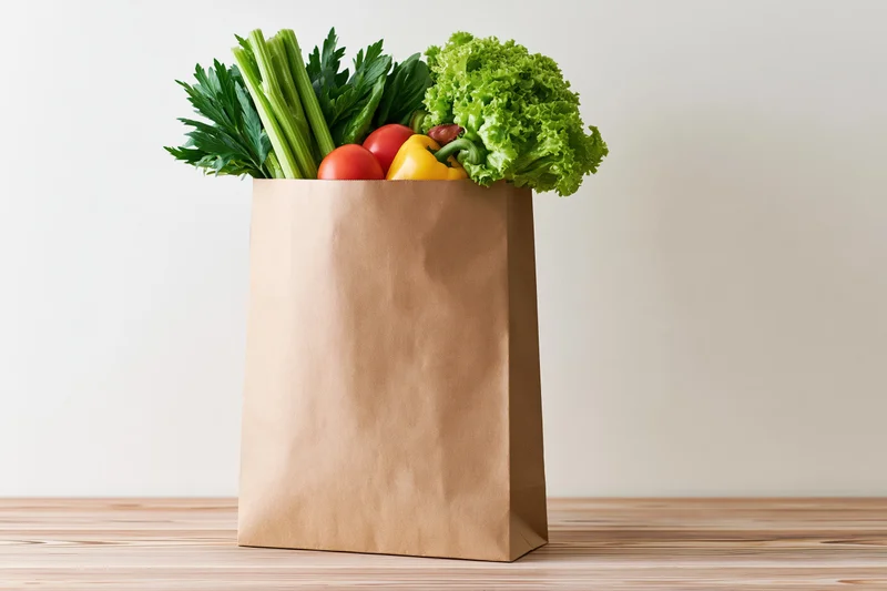 Brown paper grocery bag filled with fresh vegetables on wooden table