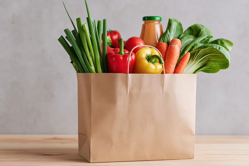 Brown paper grocery bag filled with fresh vegetables on wooden table