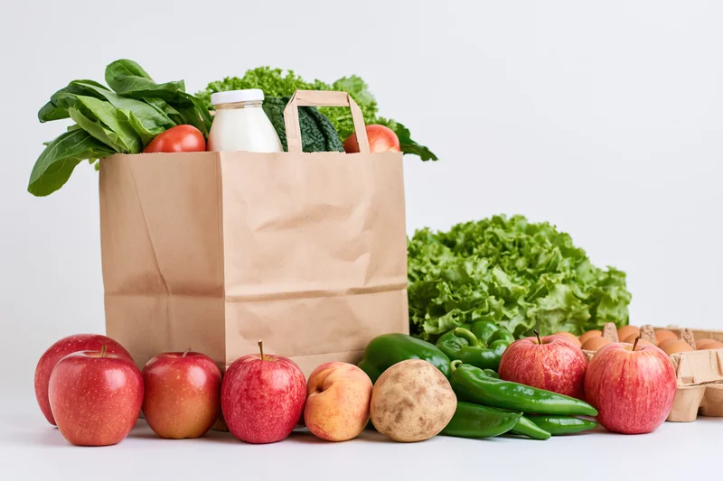 Brown paper grocery bag filled with fresh vegetables and fruits on white background