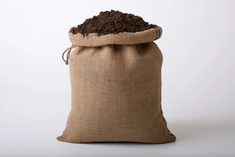 Burlap sack filled with dark brown potting soil on white background