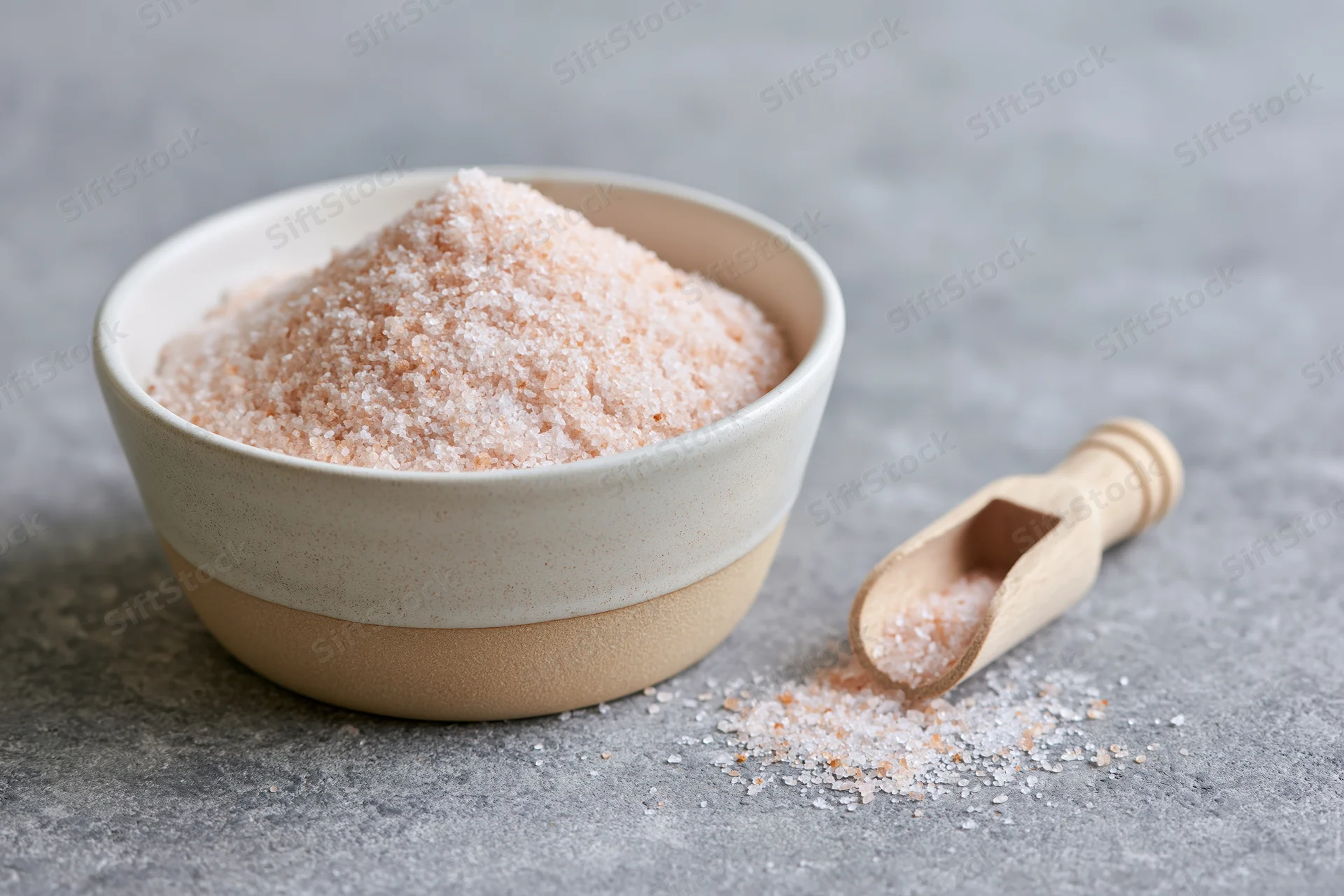 Pink himalayan salt in a ceramic bowl with a wooden spoon on a gray surface
