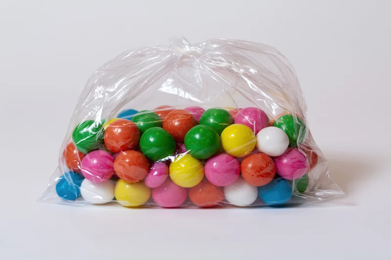 Clear plastic bag filled with colorful round gumballs on white background