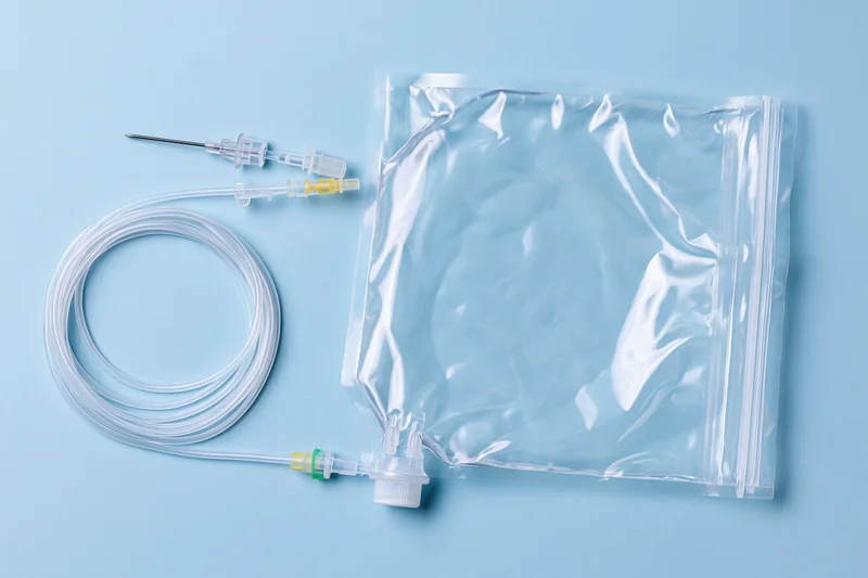 Clear plastic iv saline bag with coiled tubing and needle connector on blue background