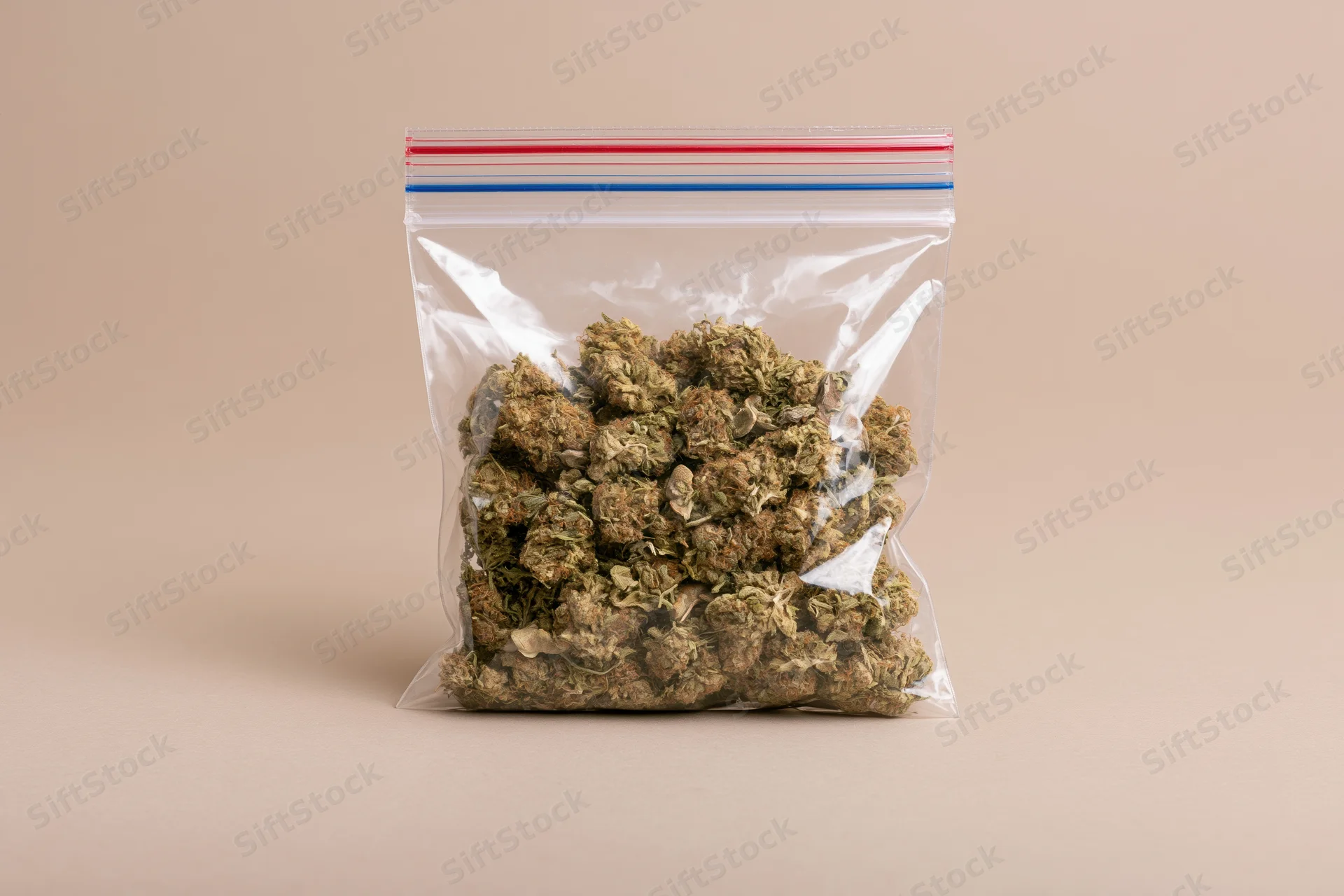 Dried cannabis buds in a clear resealable plastic bag on a beige surface