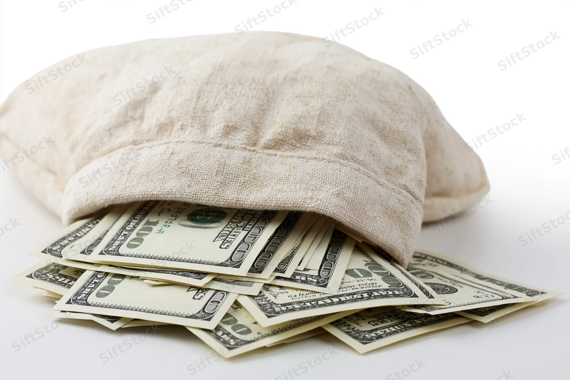 Cream canvas money bag tipped on its side spilling US hundred-dollar bills onto white surface