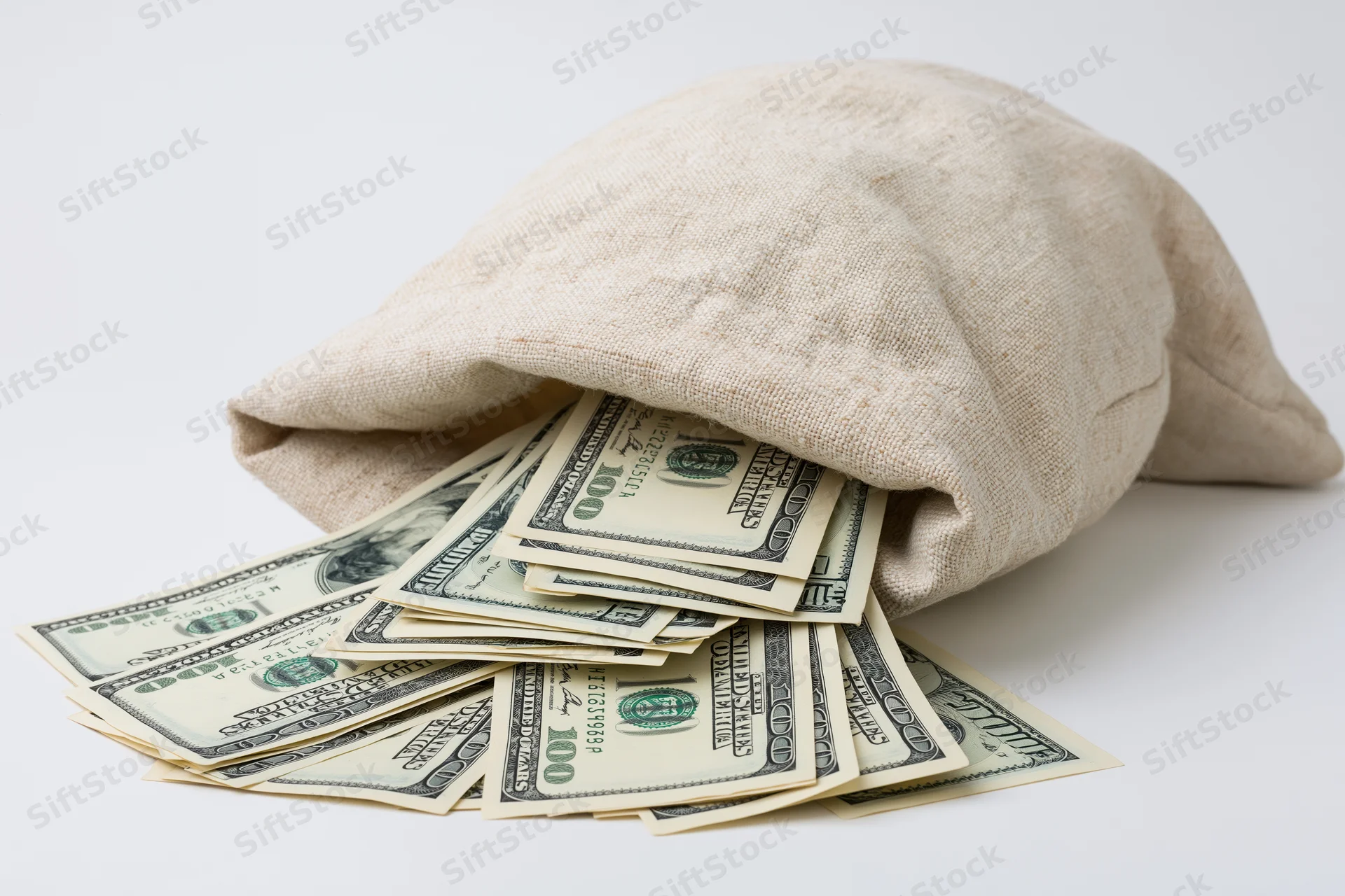 Cream canvas bag tipped over spilling hundred-dollar bills on white surface