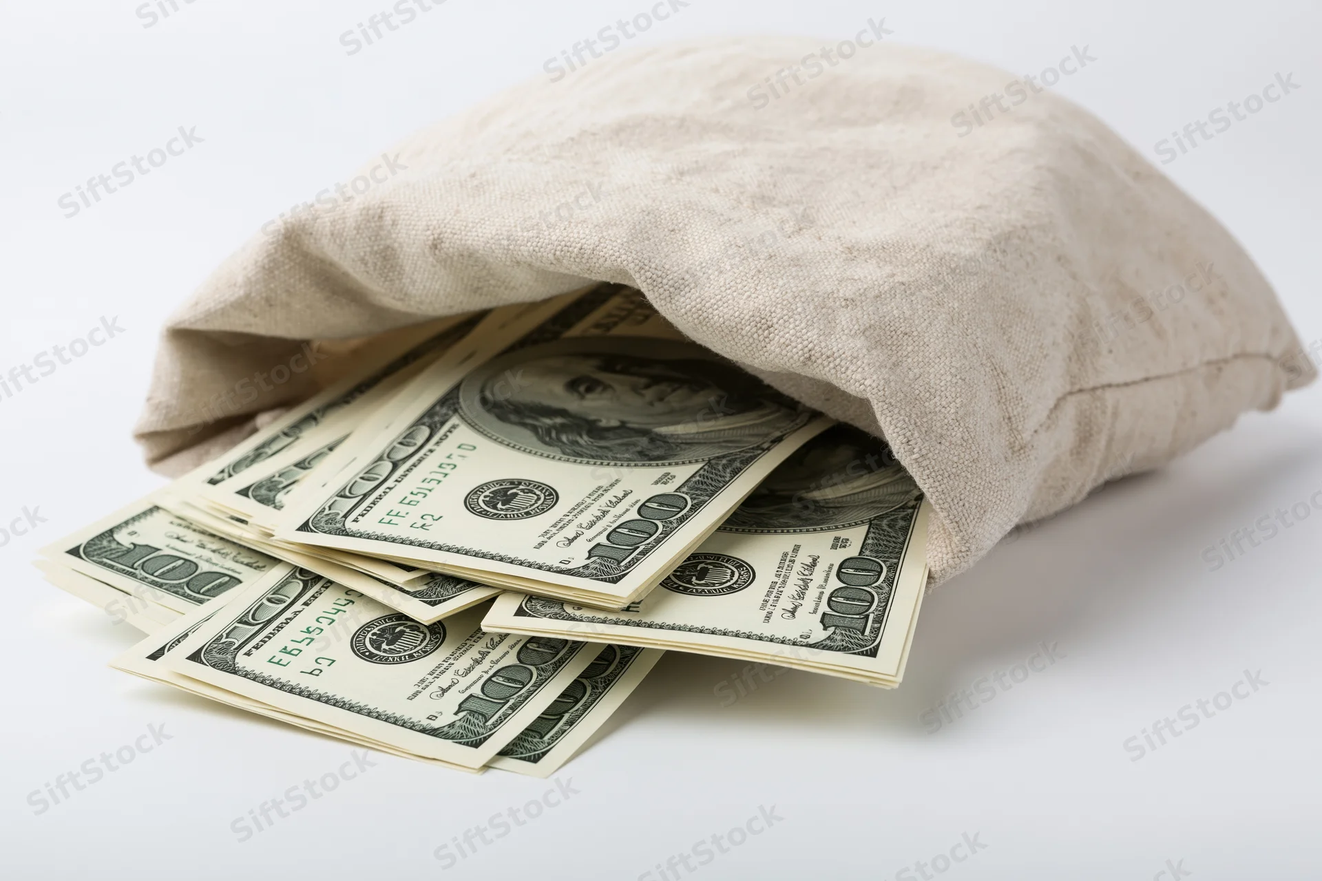 Cream canvas money bag tipped on its side spilling hundred-dollar bills onto white surface