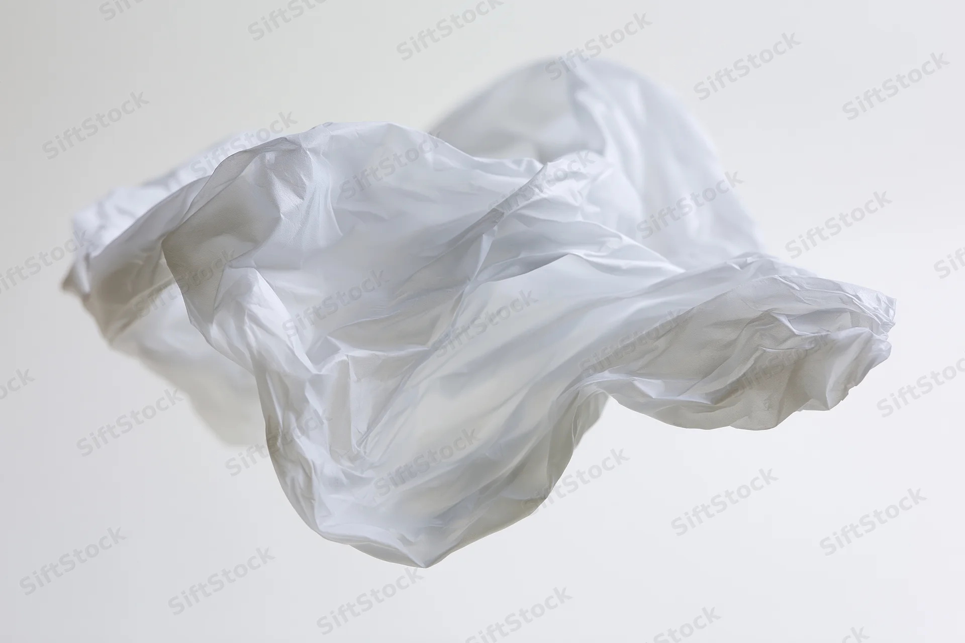 Crumpled white plastic bag floating midair against plain background