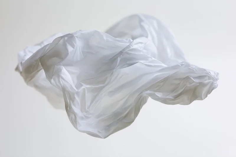 Crumpled white plastic bag floating midair against plain background