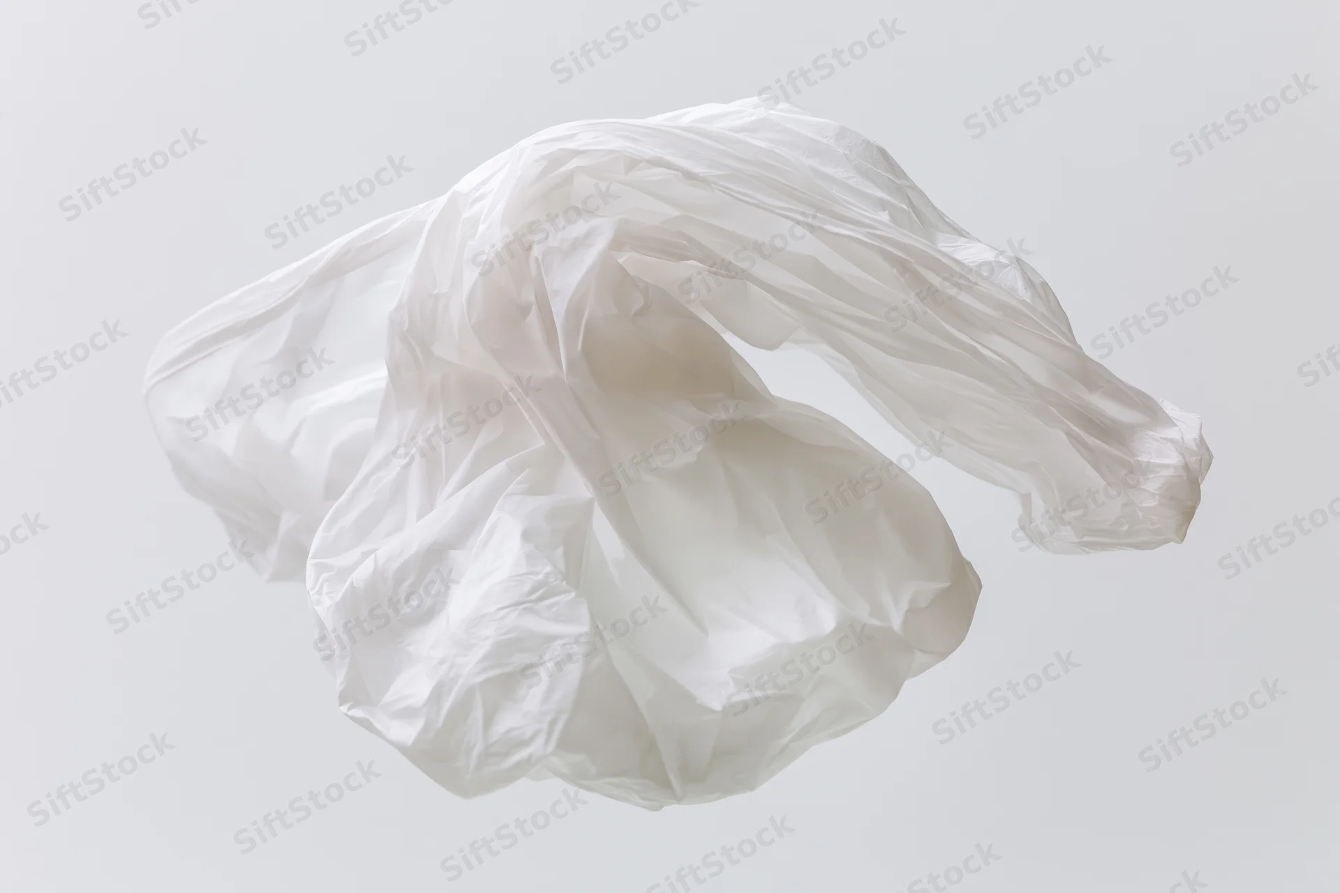 Crumpled white plastic bag floating midair against plain background