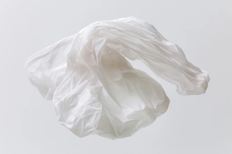 Crumpled white plastic bag floating midair against plain background