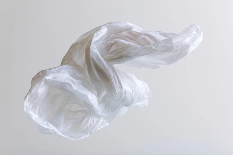 Crumpled white plastic bag floating midair against plain background