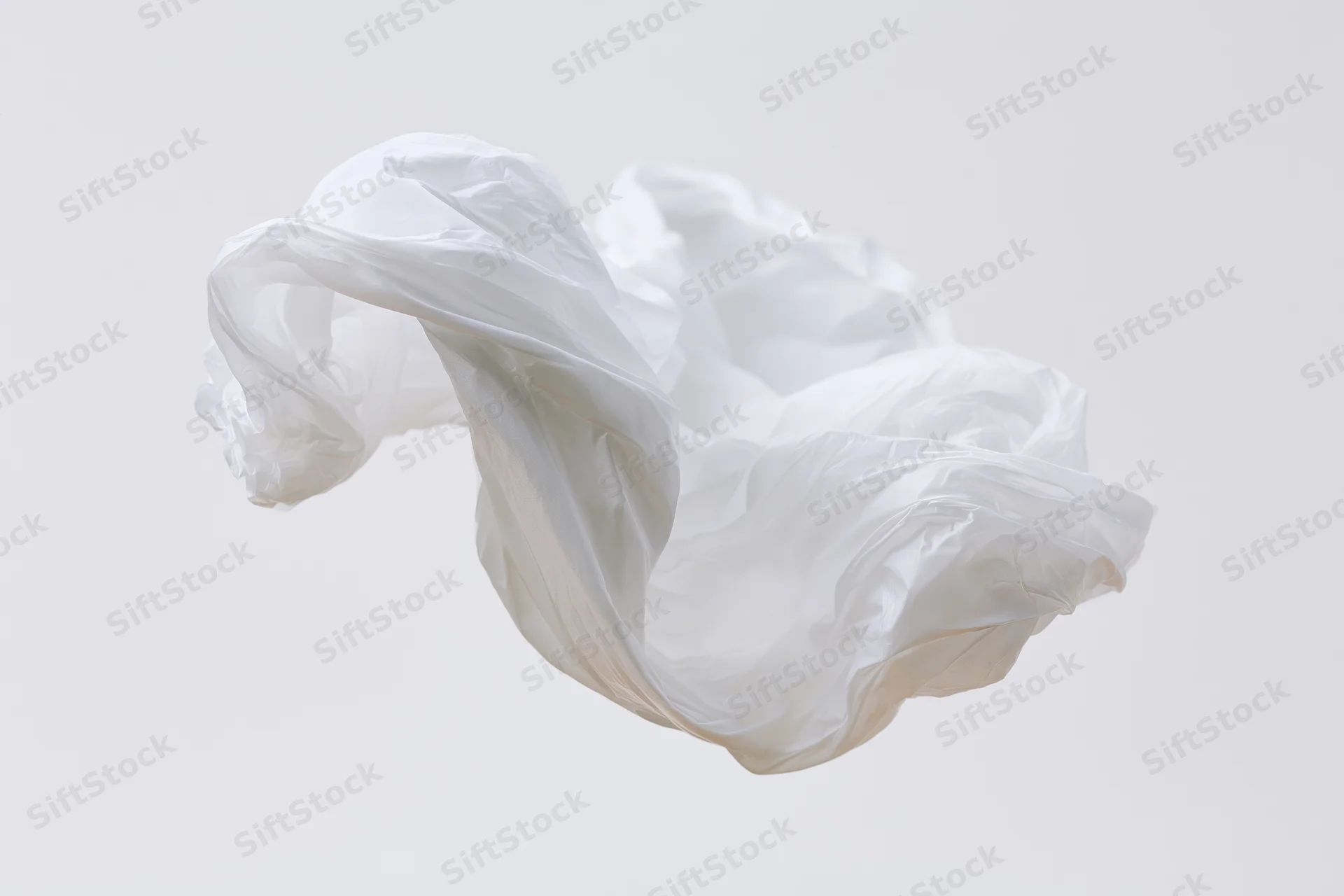 Crumpled white plastic bag floating midair against plain background