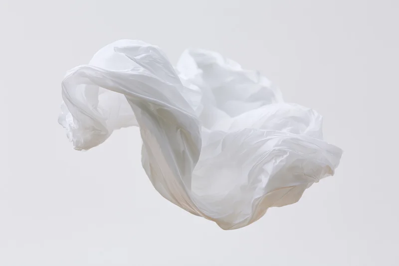 Crumpled white plastic bag floating midair against plain background