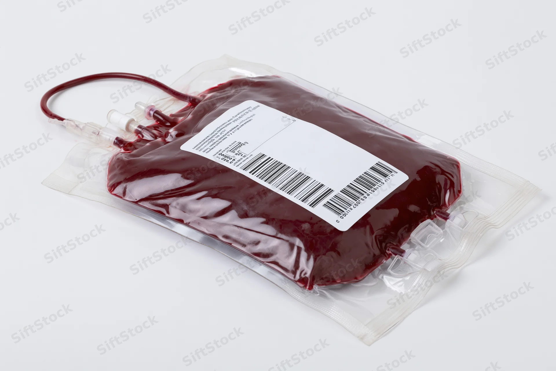 Filled medical blood donation bag with label and tubing lying flat on white surface