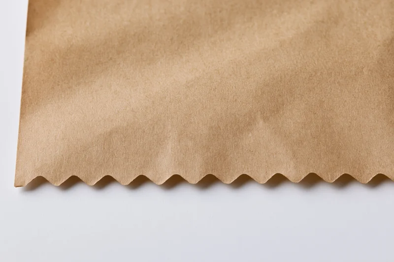 Flat kraft brown paper sheet with zigzag-cut edge on white surface