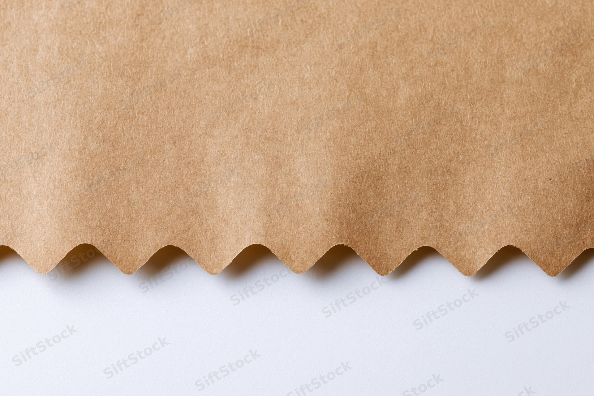 Flat kraft brown paper with zigzag-cut edge on white surface