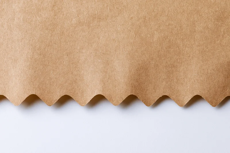 Flat kraft brown paper with zigzag-cut edge on white surface