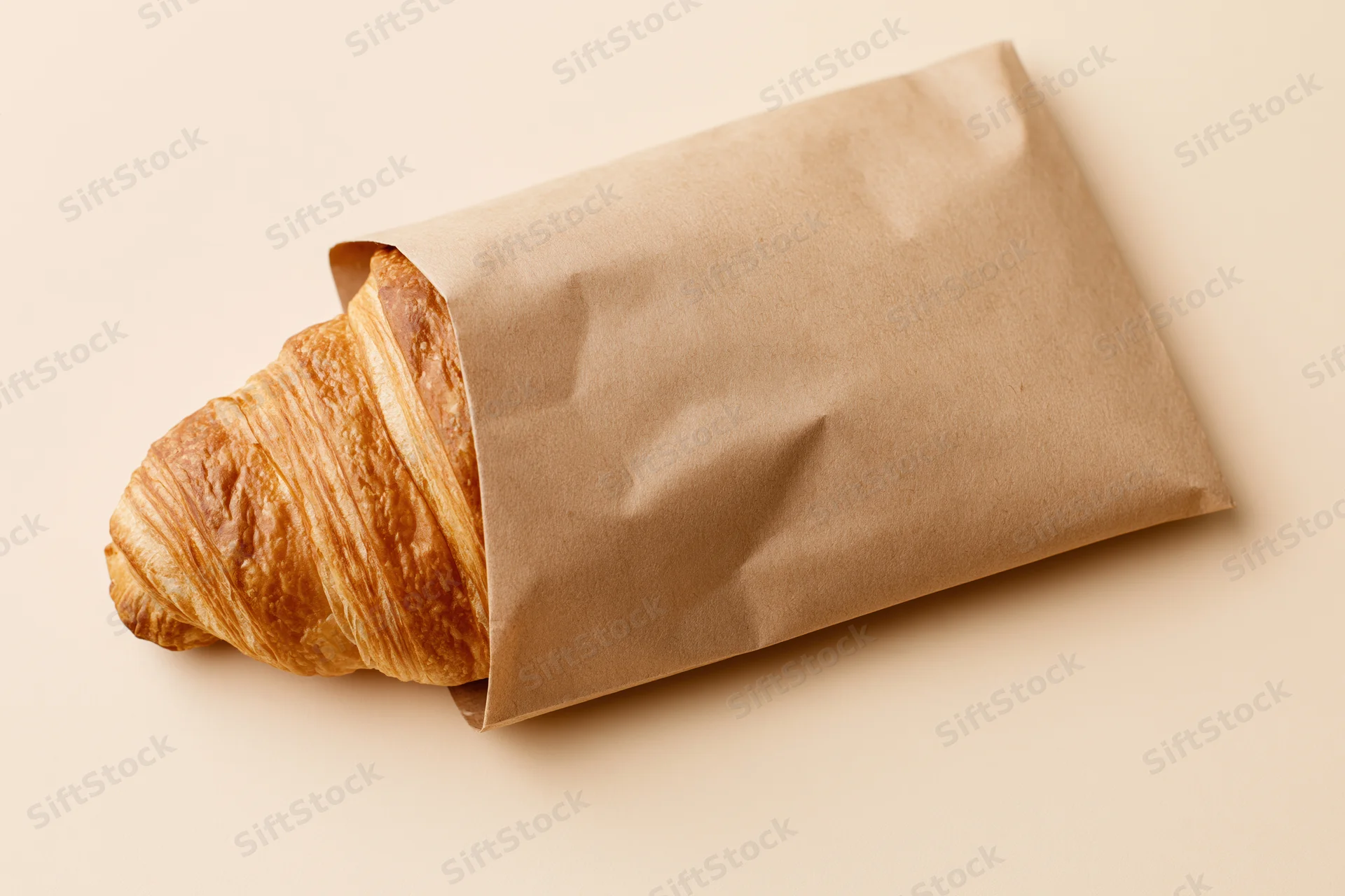 Golden croissant partially wrapped in kraft paper on a beige surface