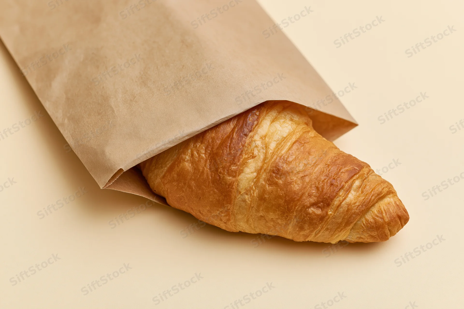 Golden croissant partially wrapped in kraft paper on a neutral surface