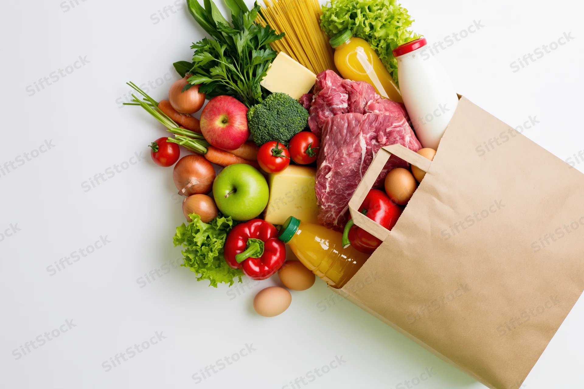 Kraft paper grocery bag tipped on its side spilling fresh produce, meat, dairy and pantry staples onto white surface