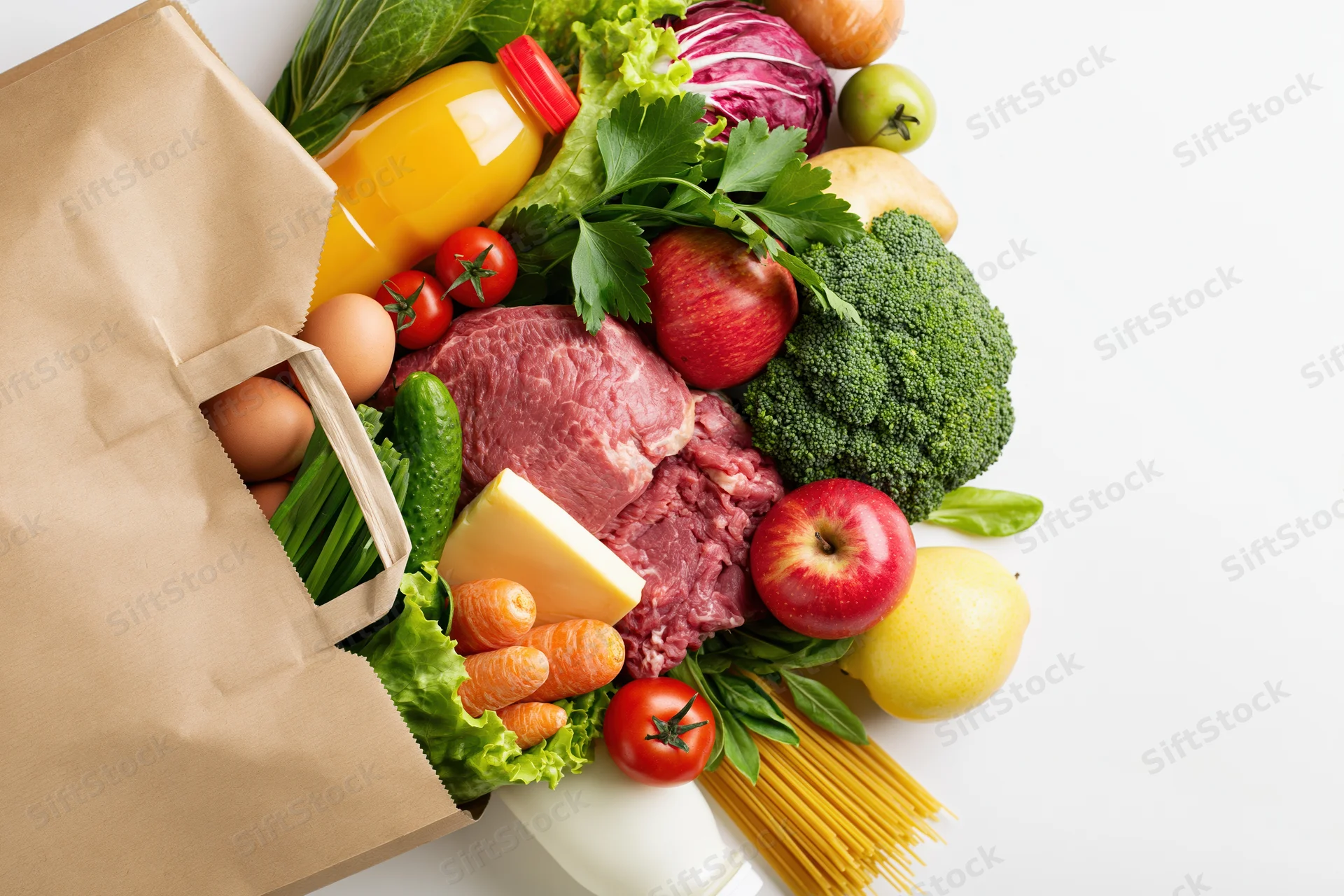 Kraft paper grocery bag tipped over spilling fresh produce, meat, dairy and pantry staples onto white surface