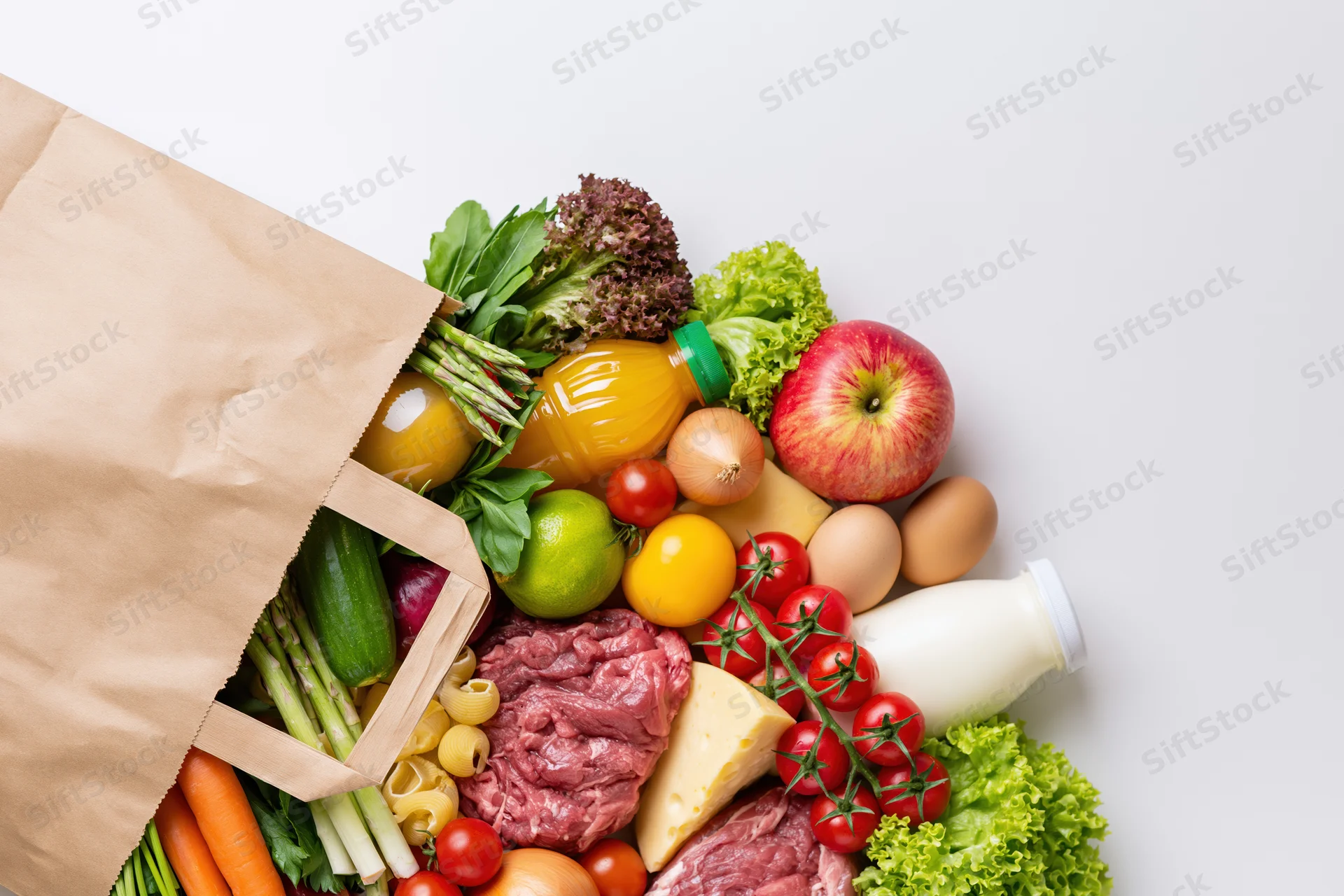 Kraft paper grocery bag tipped over spilling fresh produce, meat, dairy and pantry items onto white surface