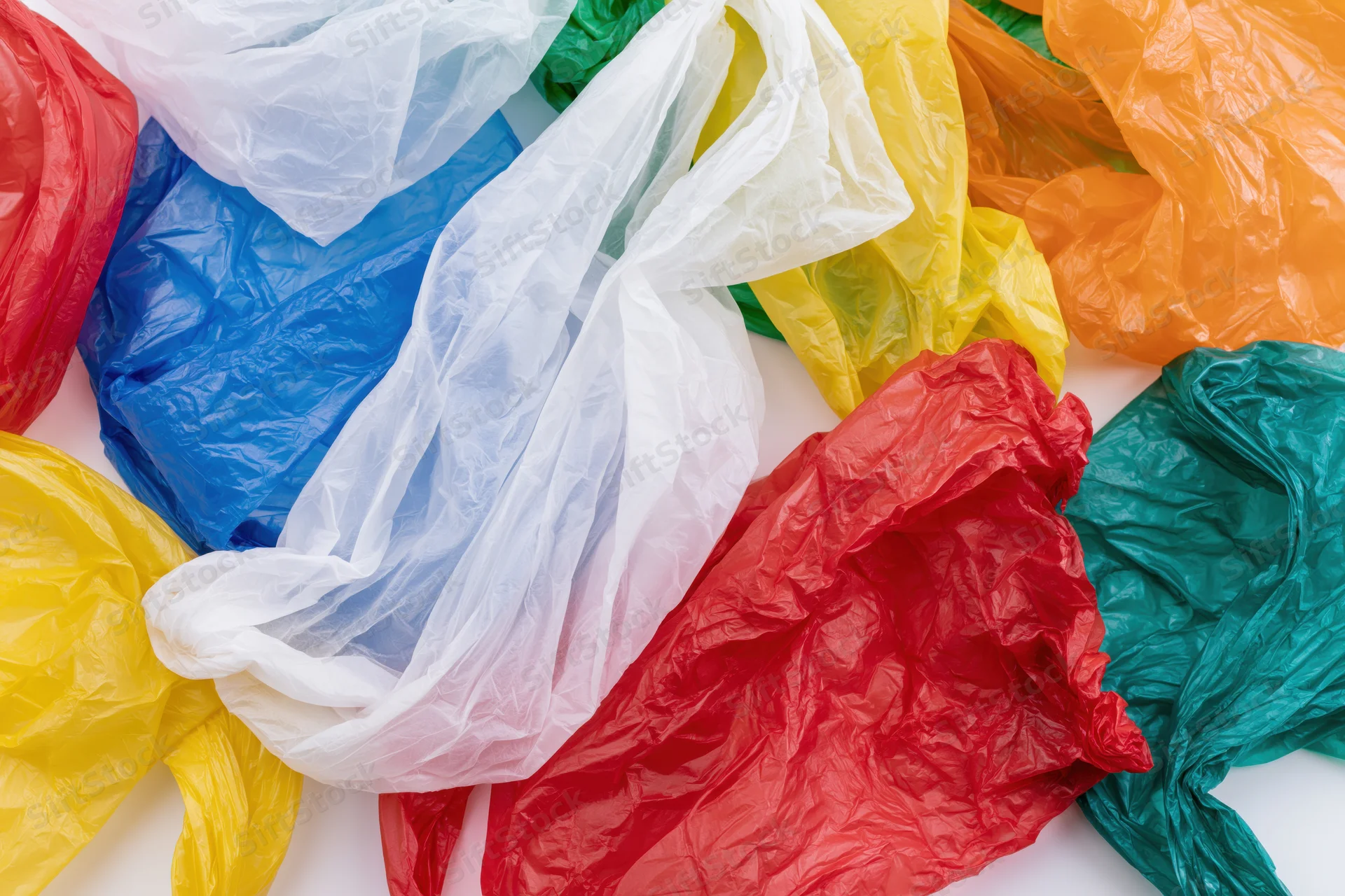 Crumpled plastic shopping bags in multiple colors scattered on white surface