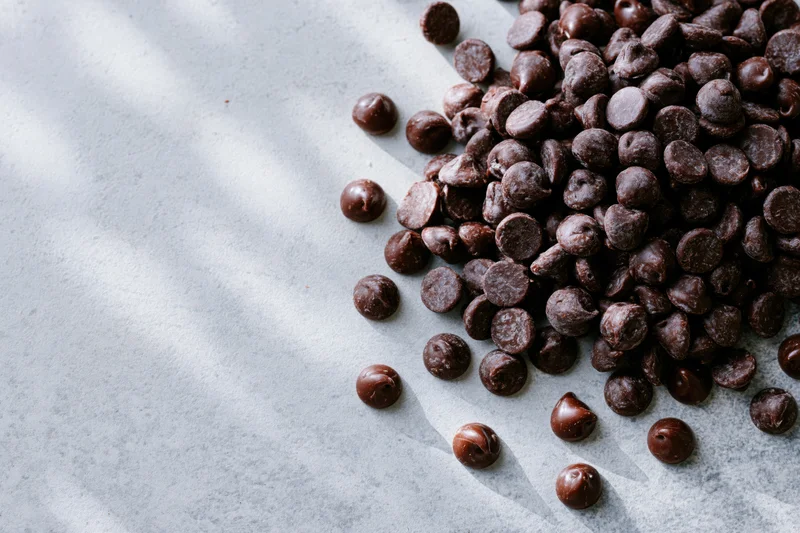 Chocolate chips scattered on a gray surface with natural light and shadows, copyspace on left