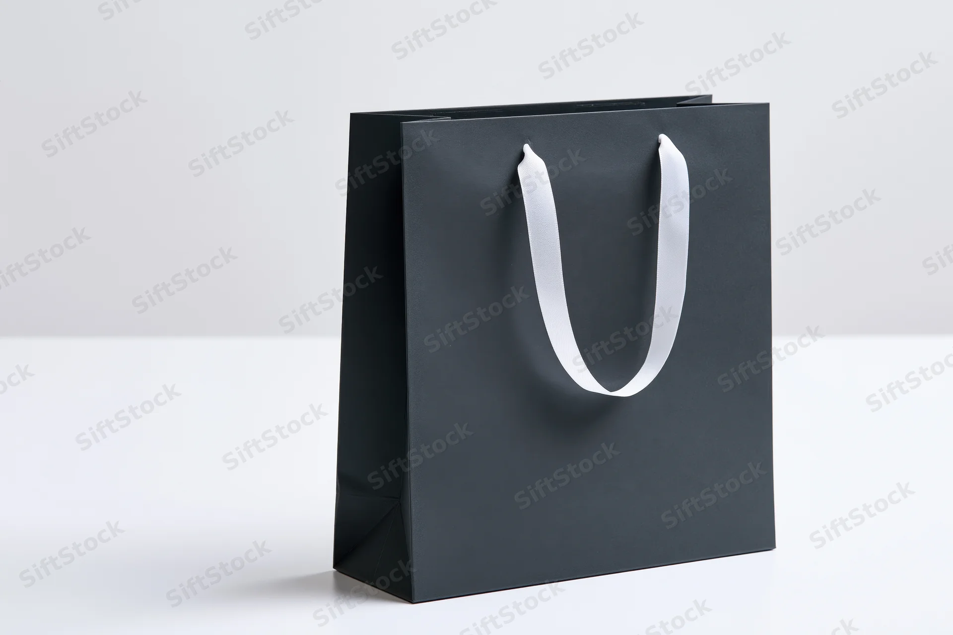 Matte black paper shopping bag with white ribbon handles on white surface