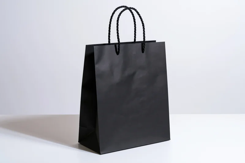 Black paper shopping bag with twisted cord handles on white surface