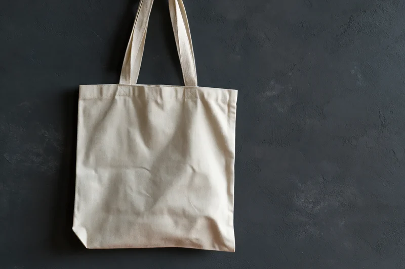 Plain canvas tote bag hanging flat against dark textured wall