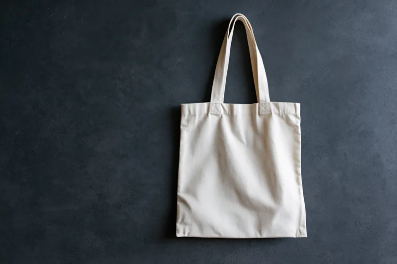 Plain canvas tote bag hanging flat against dark textured wall