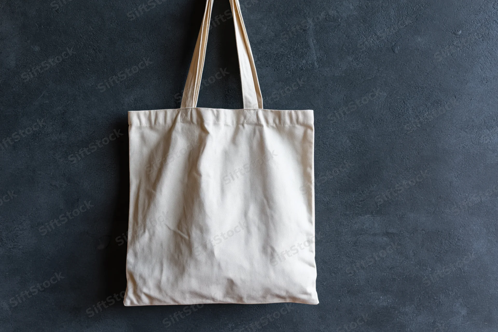 Plain canvas tote bag hanging flat against dark textured wall