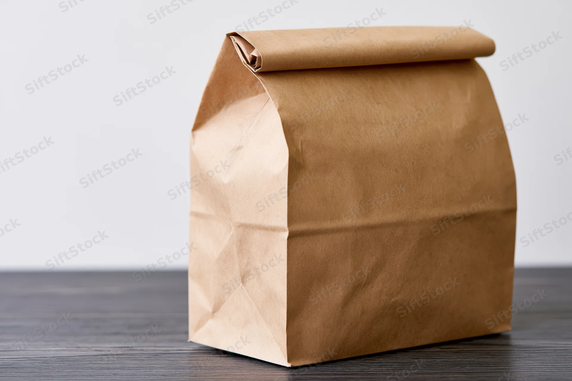 Brown kraft paper lunch bag with rolled top sitting on dark wooden table
