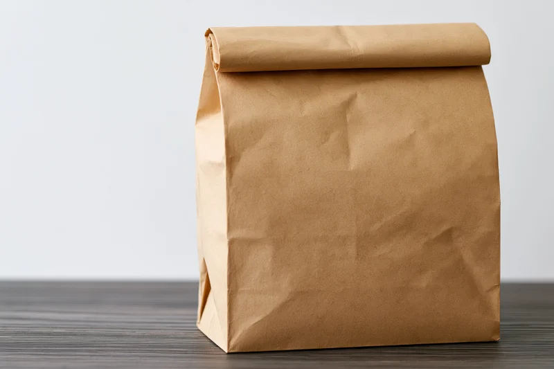Brown kraft paper lunch bag with rolled top sitting on dark wooden table