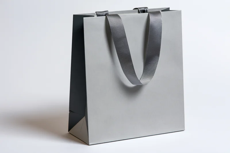 Plain grey paper shopping bag with woven fabric ribbon handles on white background