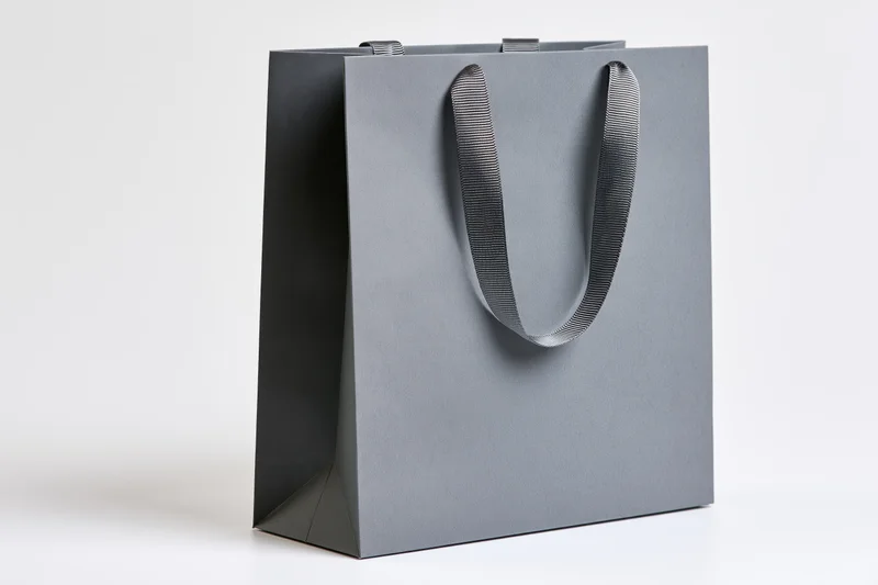 Plain grey paper shopping bag with woven fabric ribbon handles on white background