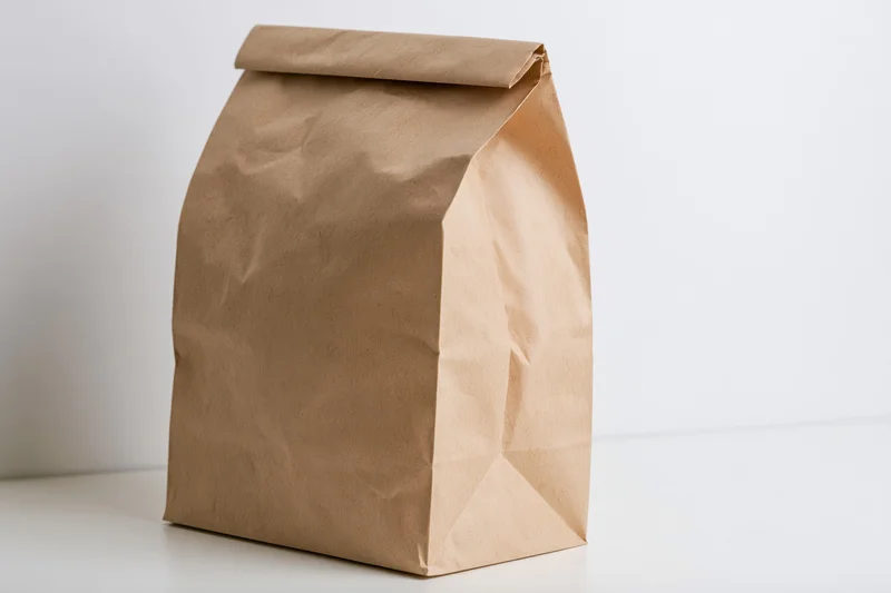 Brown kraft paper lunch bag standing upright on white surface with copyspace