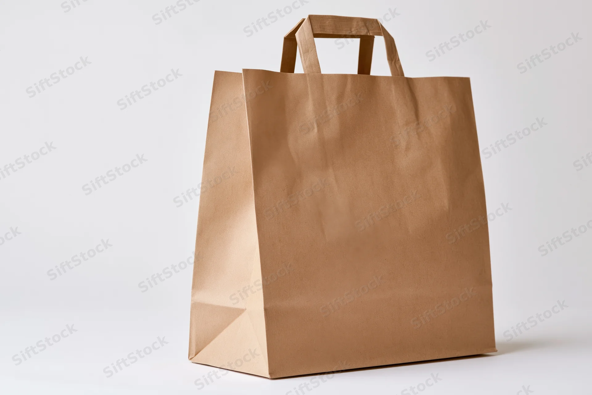 Plain kraft paper shopping bag with flat handles standing upright on white background
