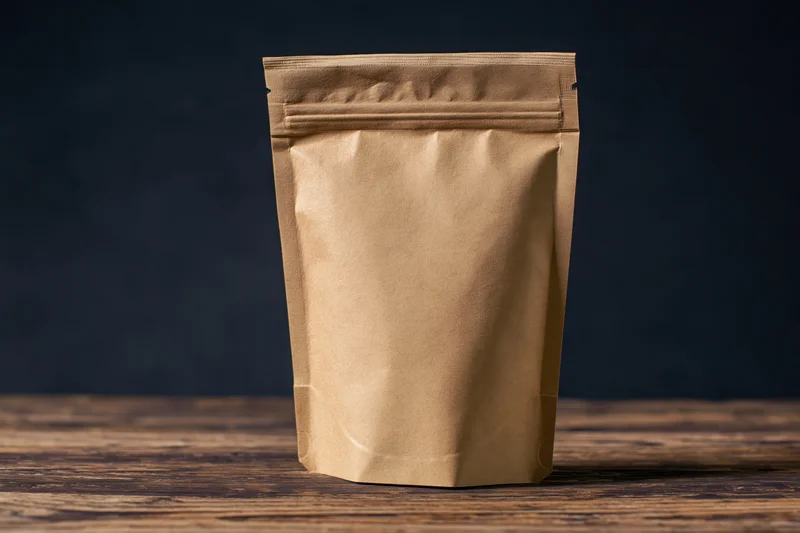 Plain kraft paper zip-top bag standing upright on a worn wooden table