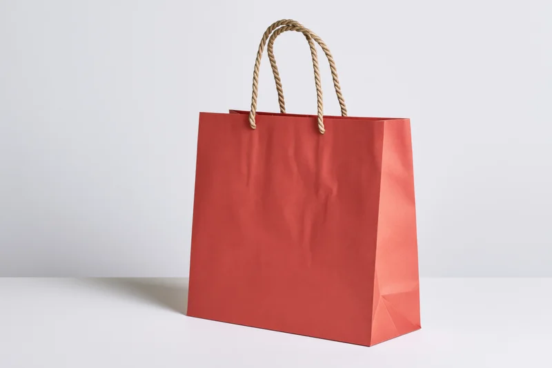 Red paper shopping bag with twisted rope handles on white surface