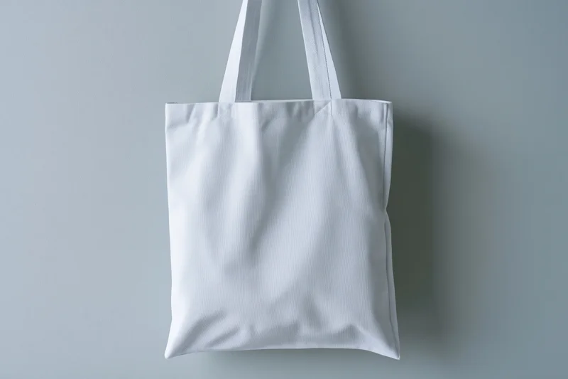 White canvas tote bag hanging upright against a gray wall