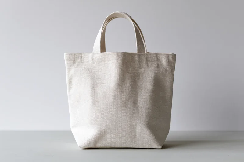 Plain white canvas tote bag standing upright on a light gray surface