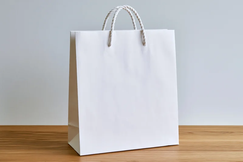 Plain white paper shopping bag with twisted rope handles on wooden table