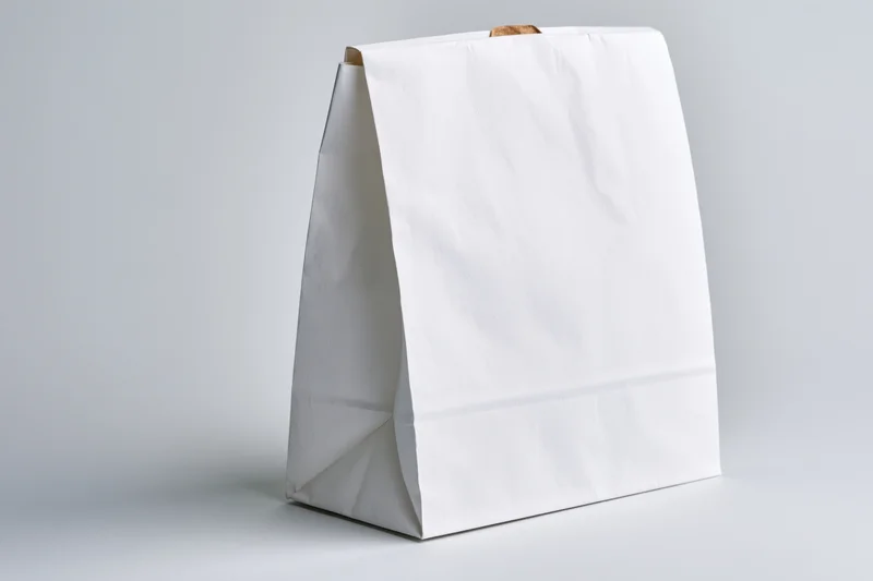 Plain white paper bag standing upright on a light surface with no print or branding