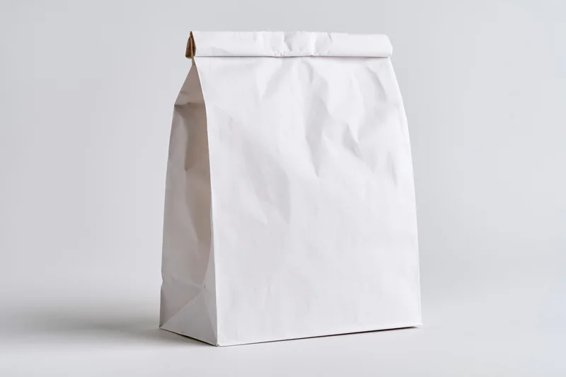 Plain white paper bag standing upright and empty on a white surface