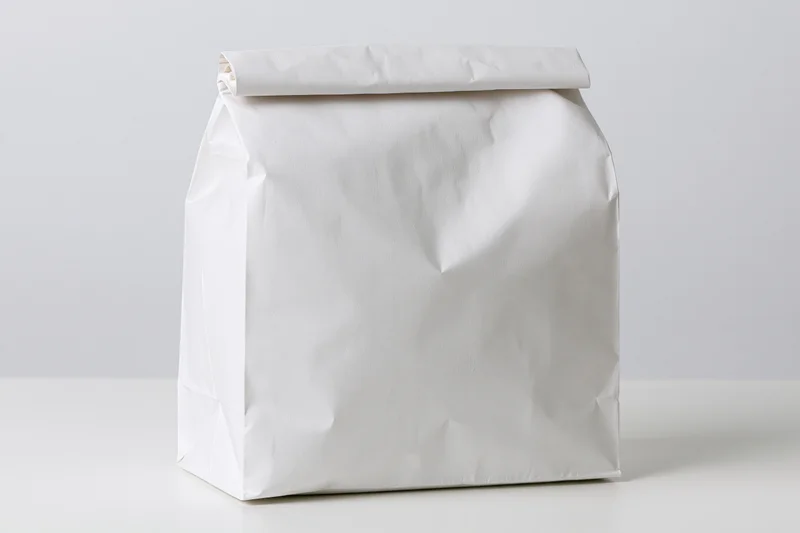 White paper bag with folded top standing upright on plain surface